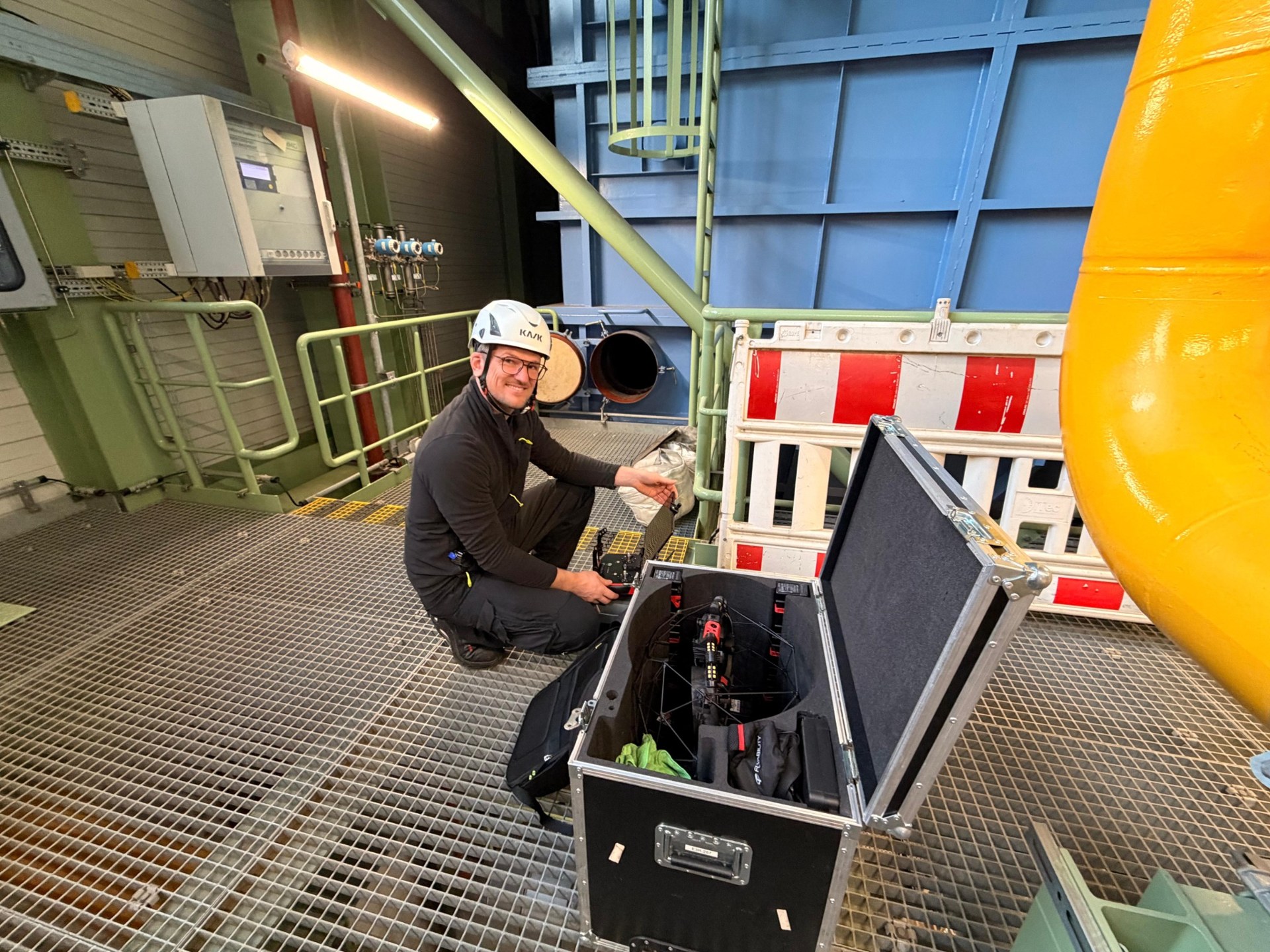 Teammitglied mit Schutzhelm bereitet die Inspektionsdrohne am geöffneten Transportkoffer in einer Anlage vor