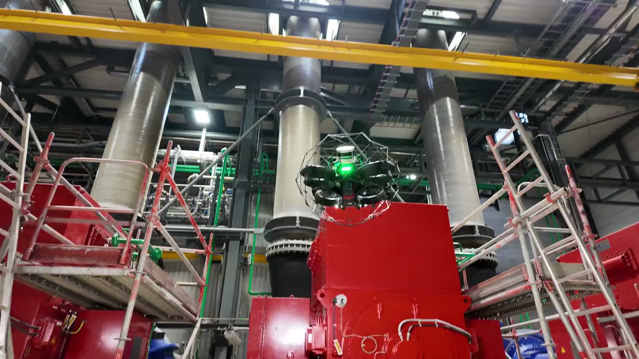 Inspektionsdrohne im Schutzkäfig in einer Maschinenhalle zwischen Gerüst und senkrechten Rohren