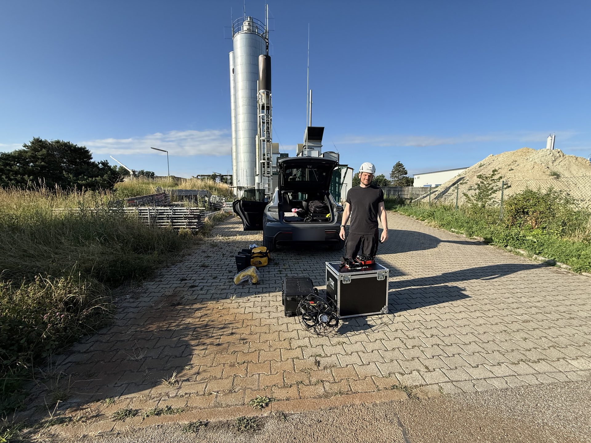 Einsatztechniker Stefan Wolf mit Helm neben dem Transportkoffer und der Elios 3 im Käfig vor einem Silo, dahinter das Einsatzfahrzeug