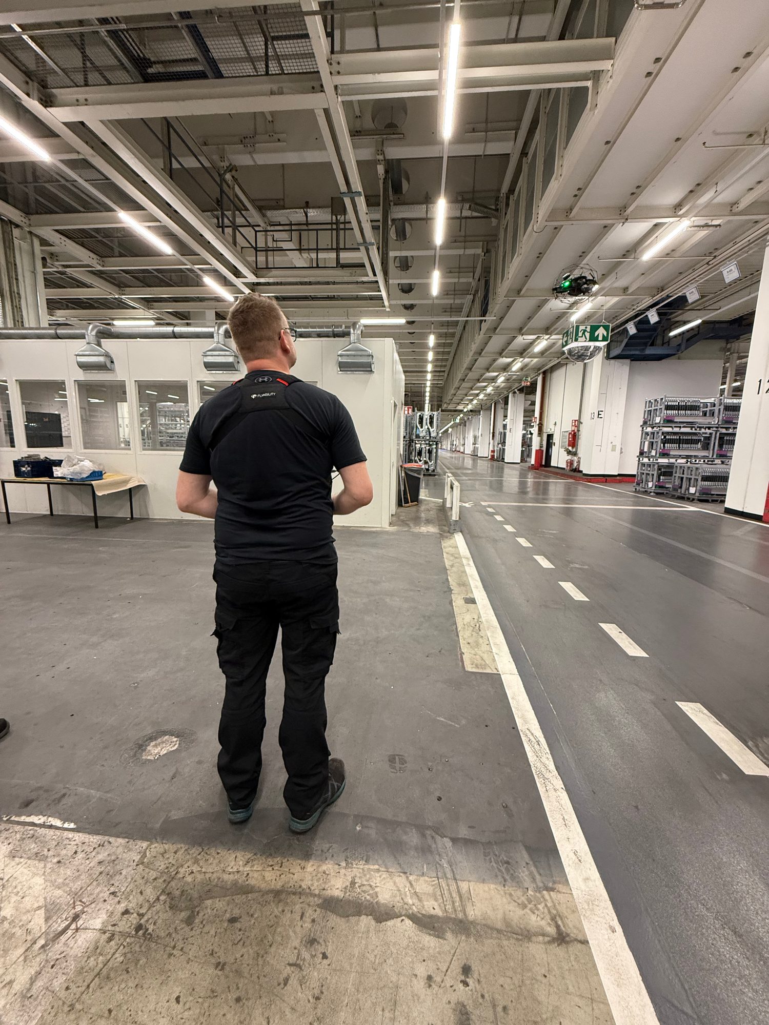 Pilot von hinten in einer langen Halle, die Drohne fliegt unter der Decke