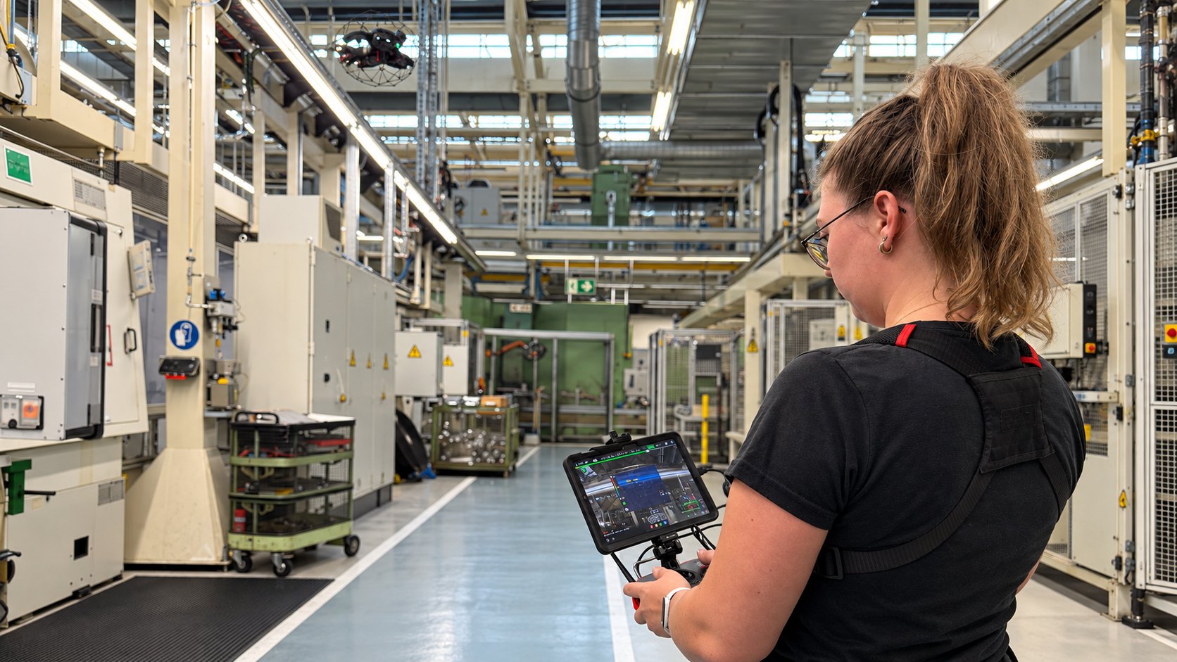 Pilotin mit Fernsteuerung und Tablet in einer Produktionshalle