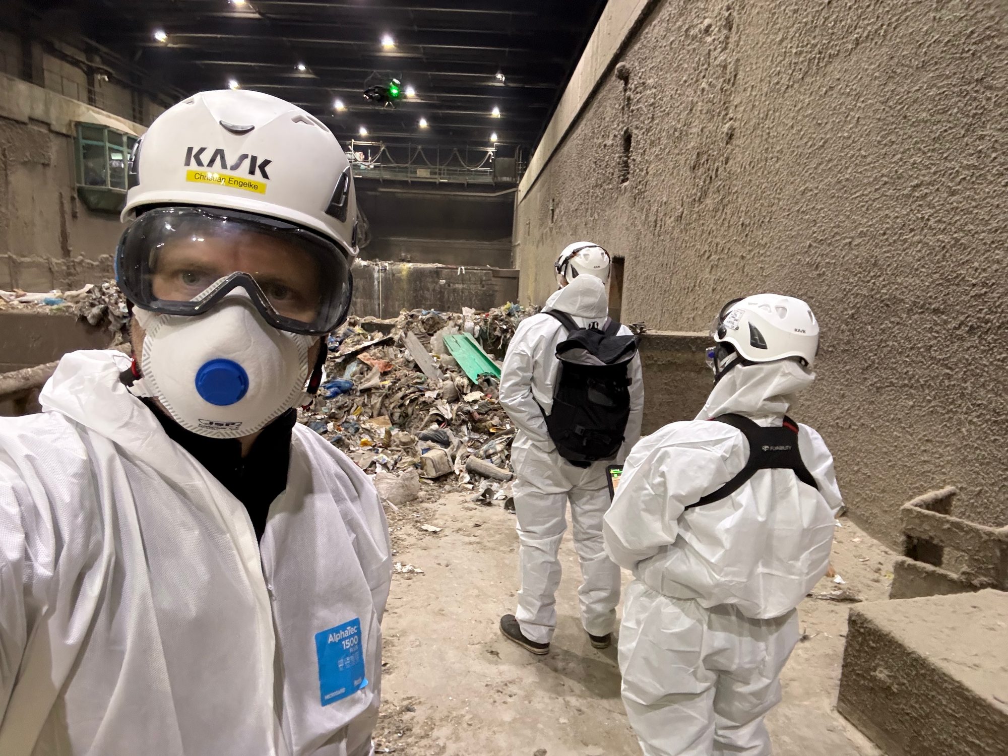 Team in weißen Schutzanzügen und Atemschutz in einem Abfallbunker