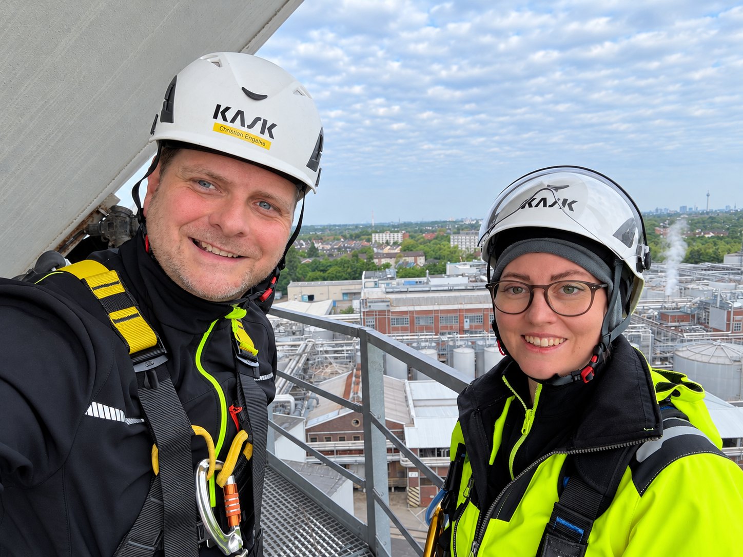 Christian Engelke und Dipl.-Wirt.-Ing. (FH) Juliana Engelke mit Schutzhelm und Auffanggurt auf einer Anlagenbühne, dahinter das Werksgelände