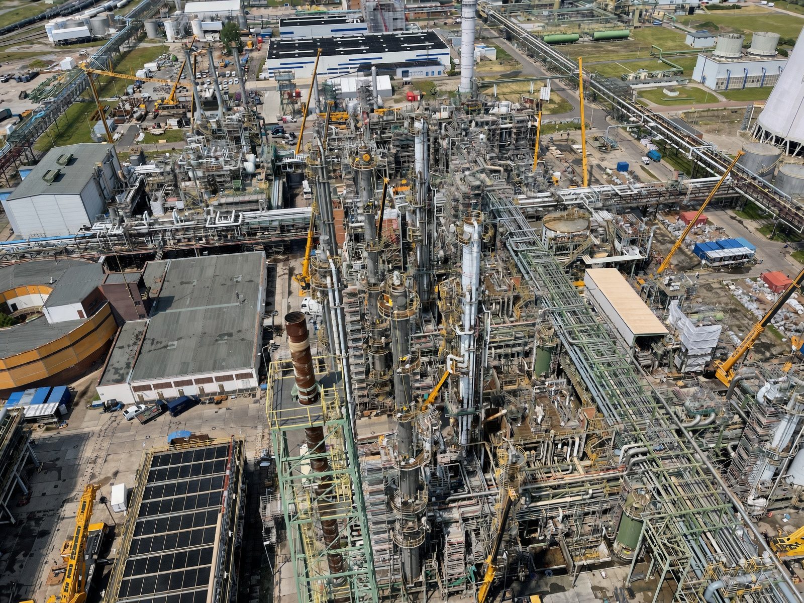 Luftbild einer Raffinerie im Turnaround: Kolonnen, Rohrbrücken und Anlagenteile mit Gerüsten, dazwischen mehrere gelbe Mobilkrane und Lagerflächen für Material