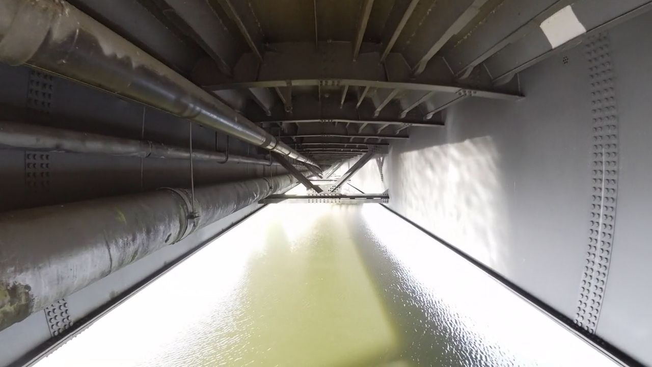 Flug zwischen Trägerwand und mehreren Leitungssträngen unter der Fahrbahnplatte einer Brücke, unten das Wasser