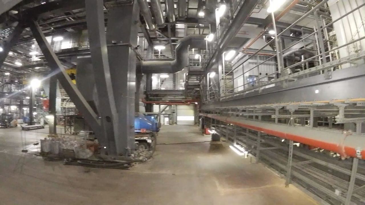 Drohnenflug durch ein Kesselhaus: Stahlstützen, Bühnen und Leitungen, über dem Hallenboden der Trichter des Kessels