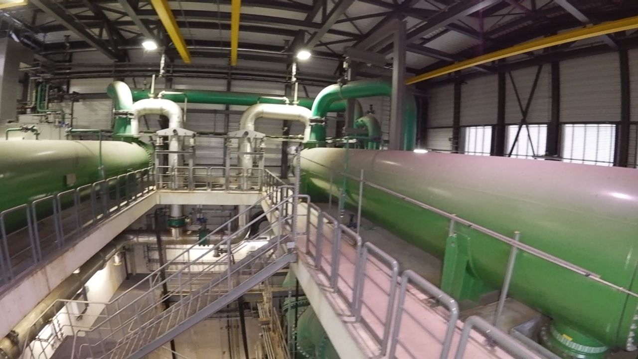 Große grüne Rohrleitungen und Pumpen in einer Halle, dazwischen Treppen und Bühnen