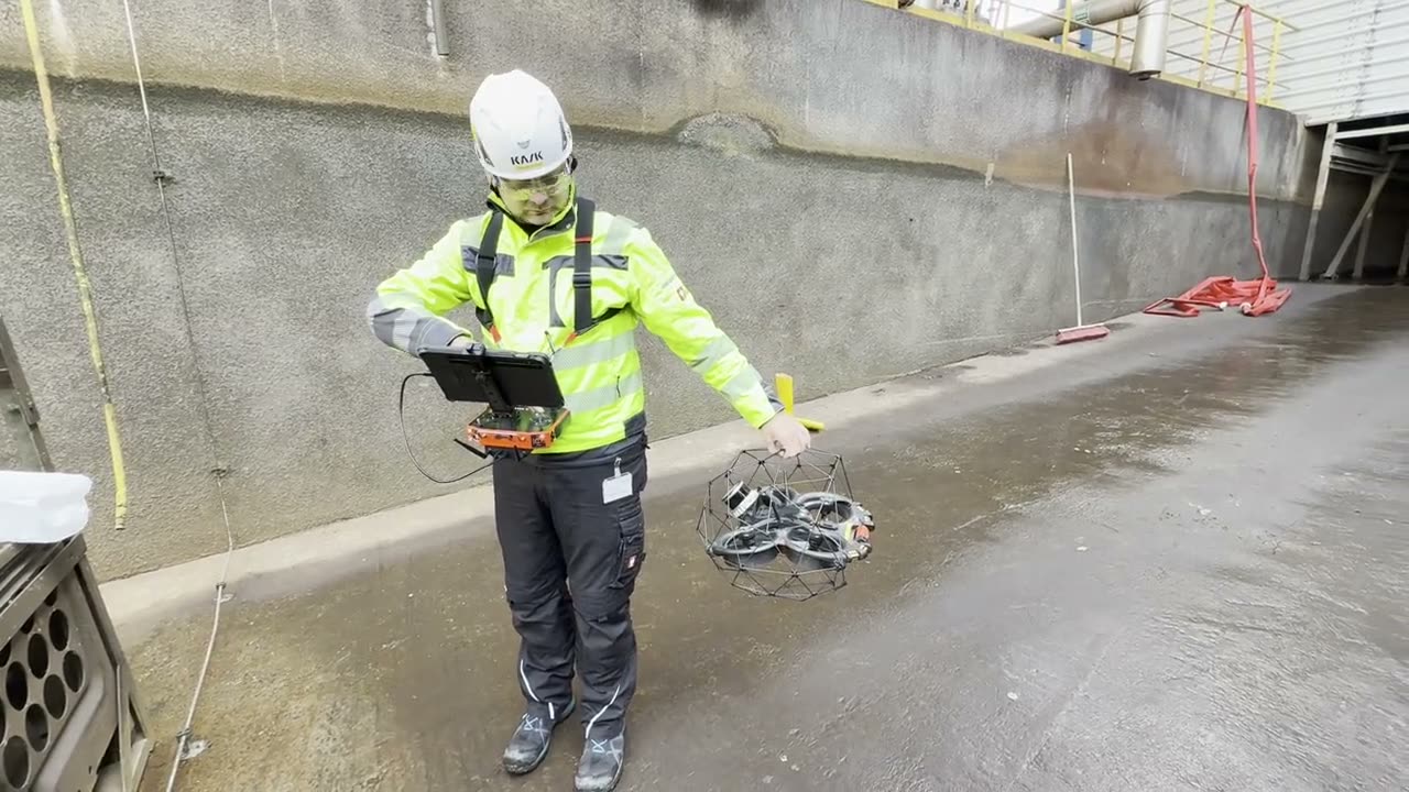 Pilot in Warnjacke mit Steuerung und Tablet hält die Inspektionsdrohne in der Kühlturmtasse