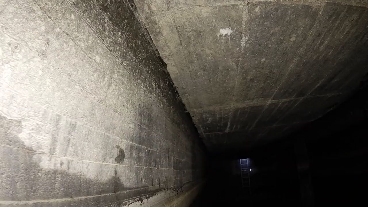 Flug unter der Betondecke an der Wand entlang, am Ende Licht an einer Steigleiter