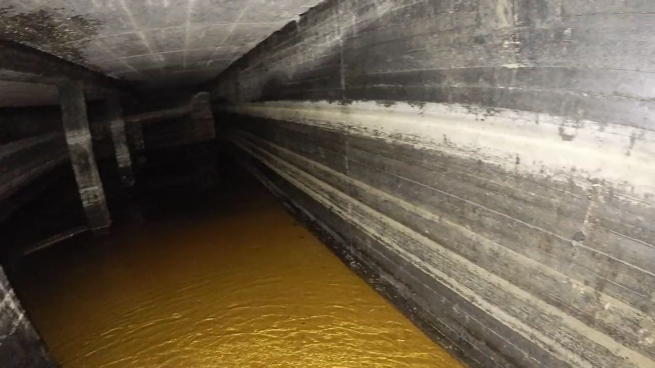 Drohnenflug durch ein unterirdisches Betonbecken: Stützen in einer Reihe, darüber die Decke, am Boden flaches Wasser